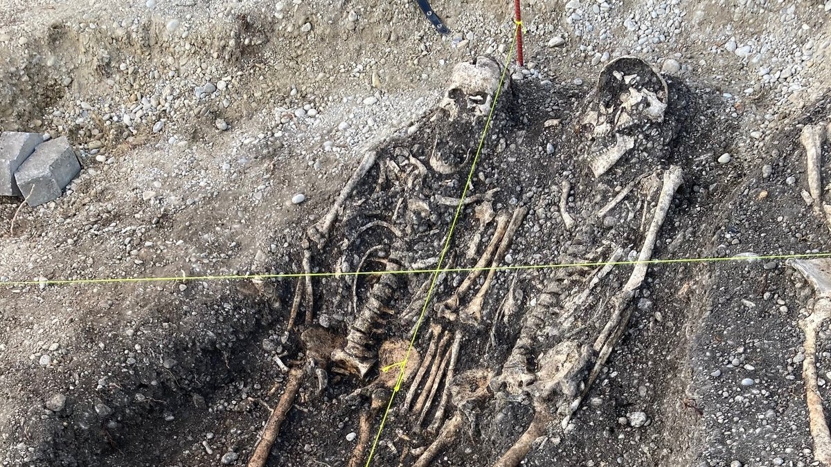 Zwei Skelette liegen freigelegt in einem von Steinen durchsetzten Boden. Ein Kreuz aus Maßbändern spannt sich darüber. Vor drei Jahren entdeckte man in Neufahrn bei Freising diese Skelette aus dem frühen Mittelalter. Sie zeigen: Der Ort ist noch älter als gedacht. (Archivbild)