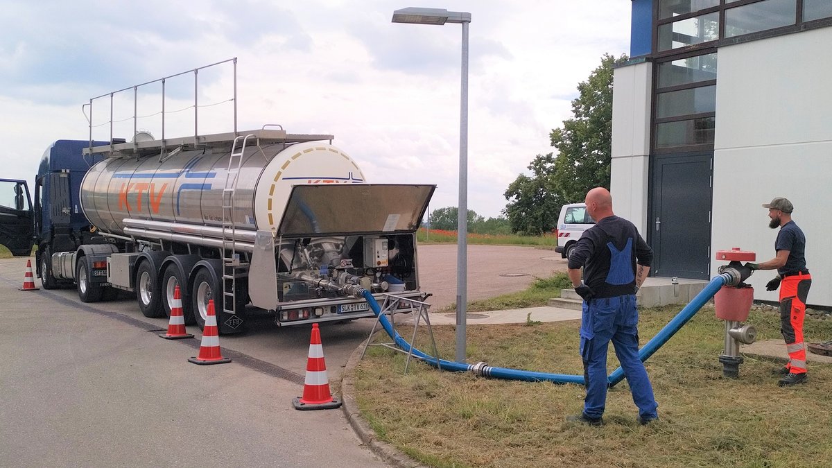 Zwei Fachkräfte pumpen Wasser aus einem Tanklaster über einen Hydranten in den Trinkwasserspeicher.