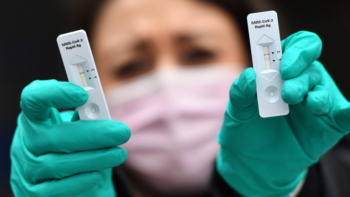 Frau mit grünen Gummihandschuhen hält zwei Coronavirus-Antigen-Tests