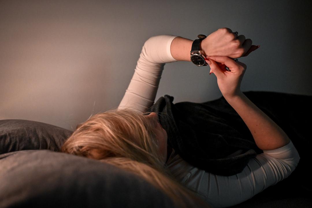 Eine Frau liegt im Bett und stellt ihre Armbanduhr (Symbolbild)