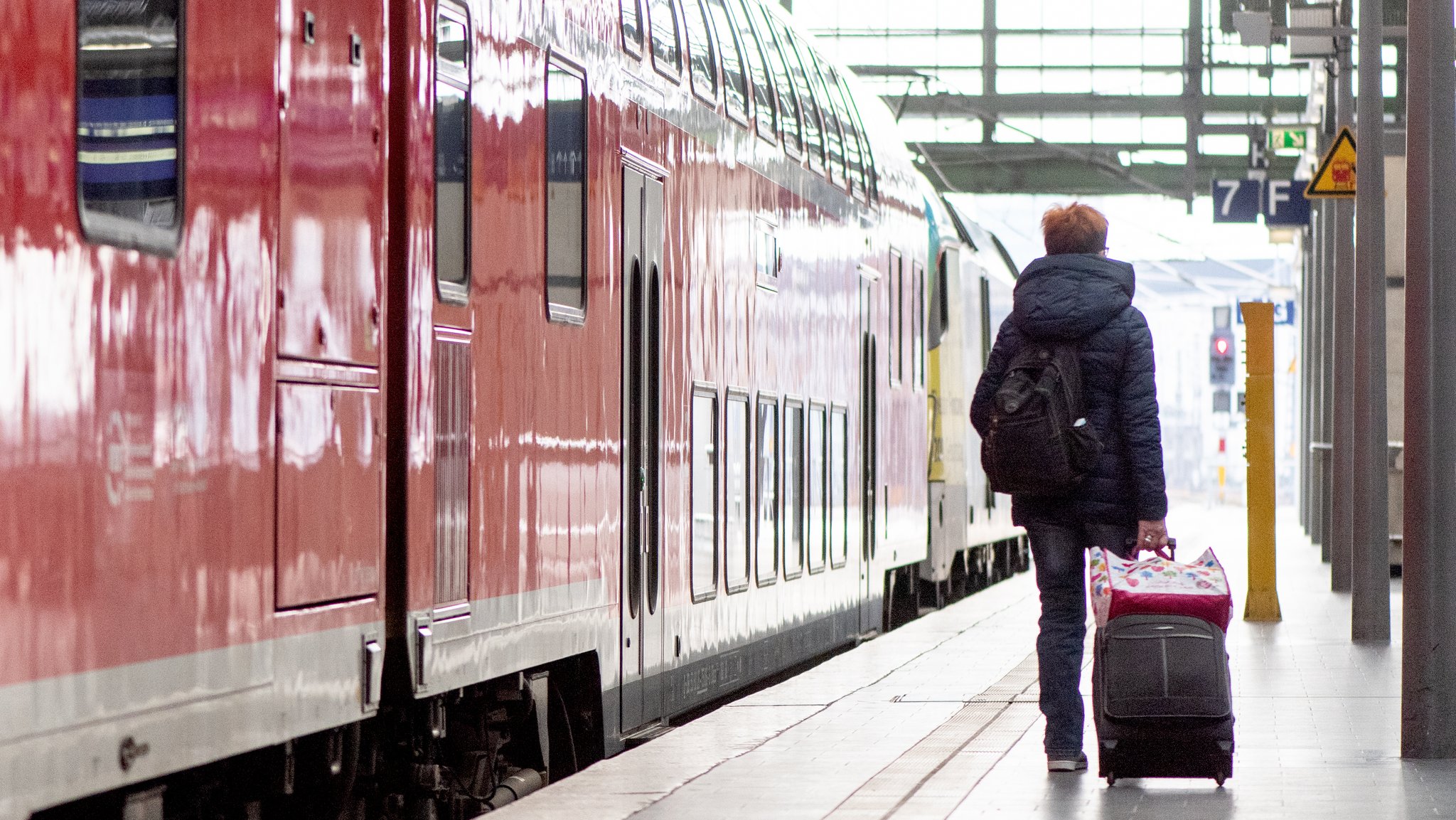 Eine Reisende läuft auf dem Bahnsteig neben einer Regionalbahn.