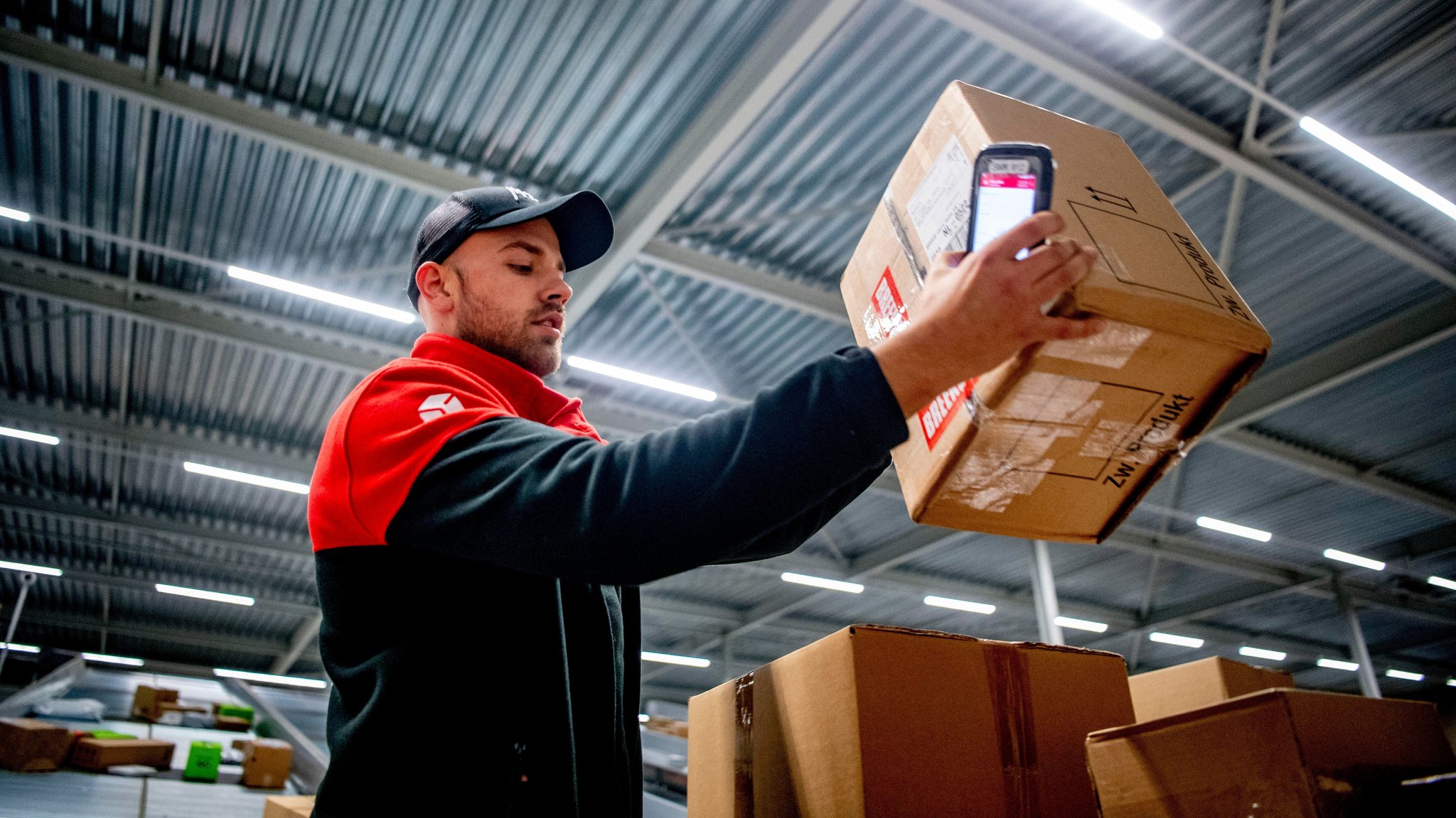 Ein Mitarbeiter von DPD hält ein Päckchen in einem Verteilzentrum in den Händen.