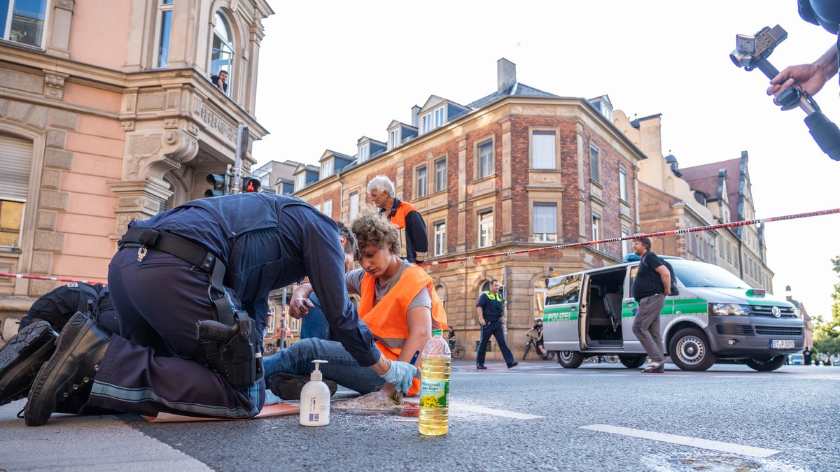 Ein Polizeibeamter löst einen Klimaaktivisten, der sich auf einer Straße festgeklebt hat, von dieser.