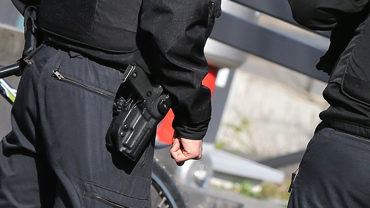 Polizisten von hinten mit Schusswaffe und kugelsicherer Weste (Symbolbild)