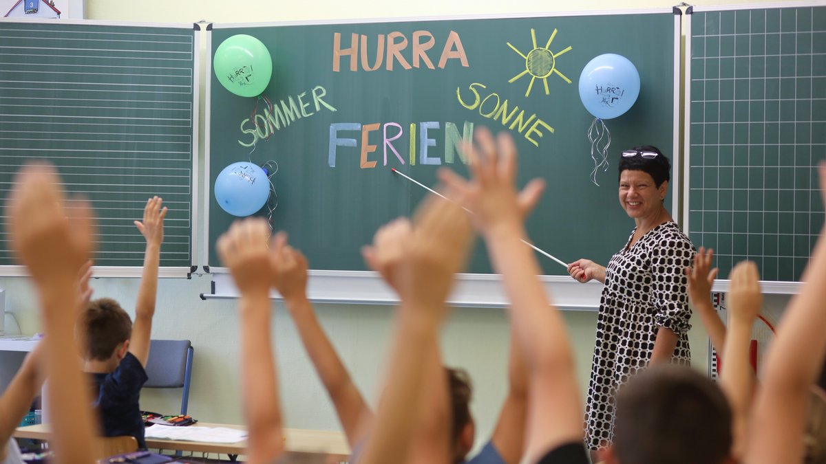 Blick in ein Klassenzimmer, an der Tafel steht: Hurra, Sommer, Sonne, Ferien.