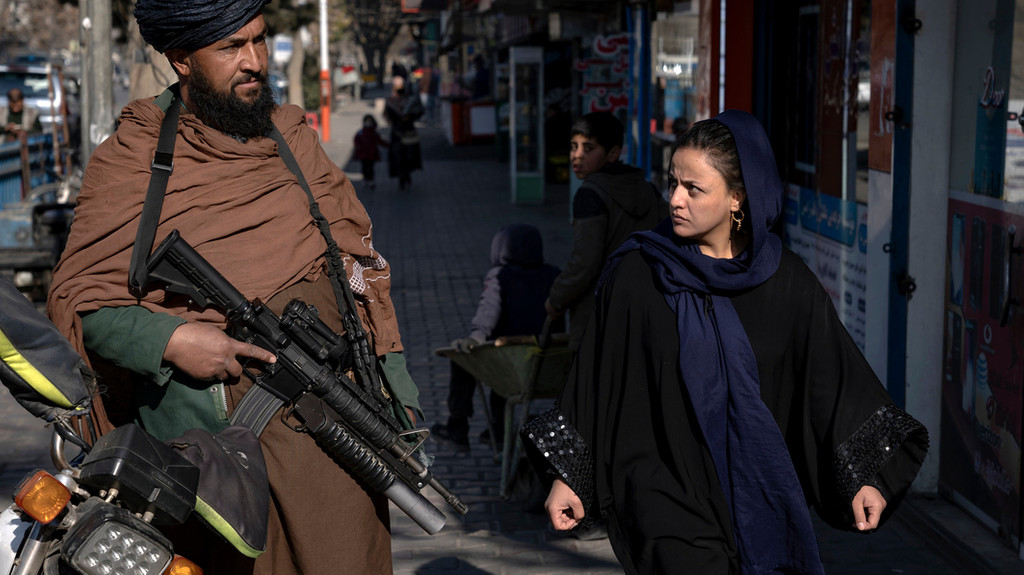 26.12.2022, Afghanistan, Kabul: Ein Taliban-Kämpfer steht Wache, während eine Frau vorbeiläuft. 