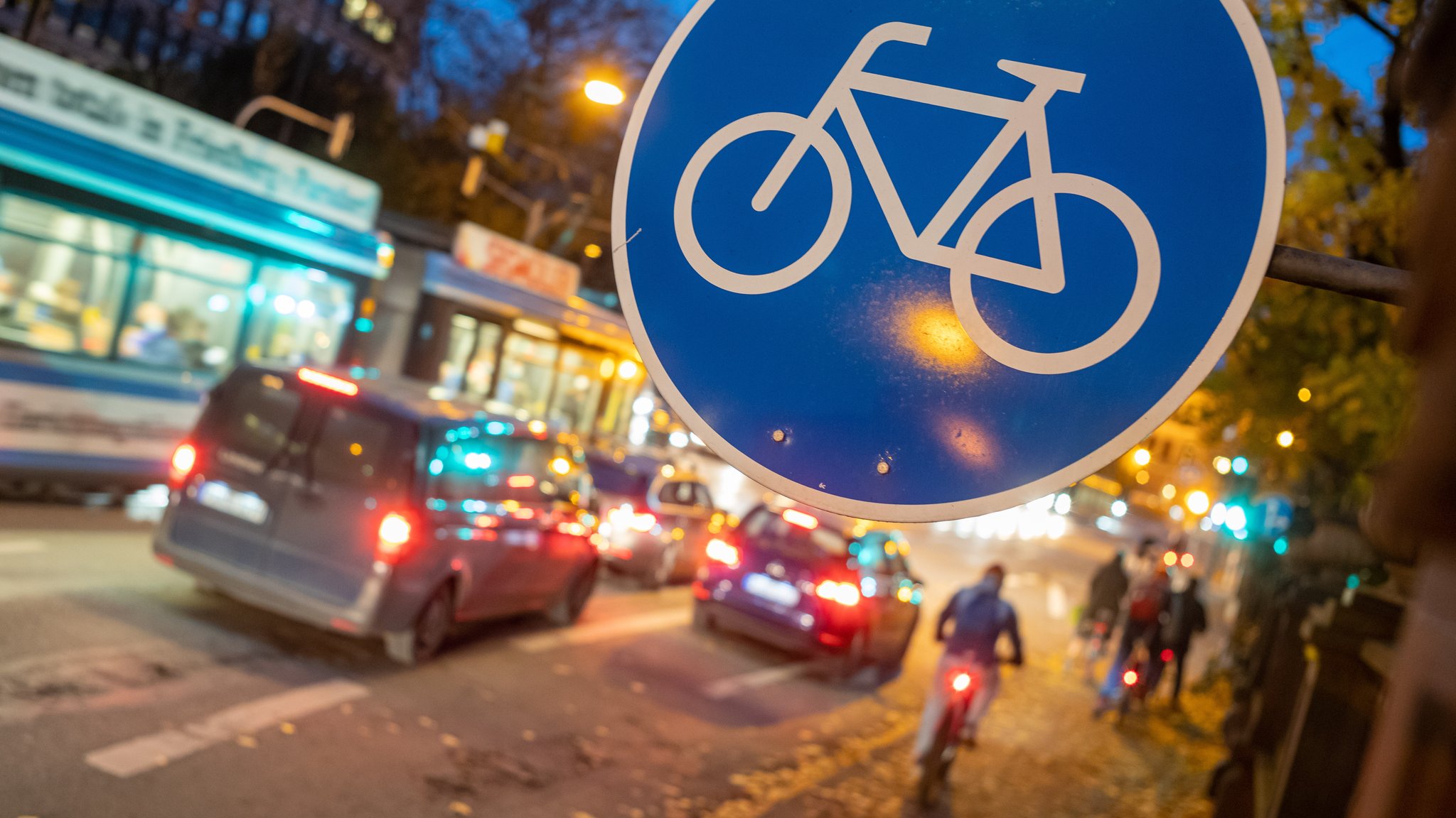 Ein Radweg-Verkehrsschild hängt am Abend über einer Straße.