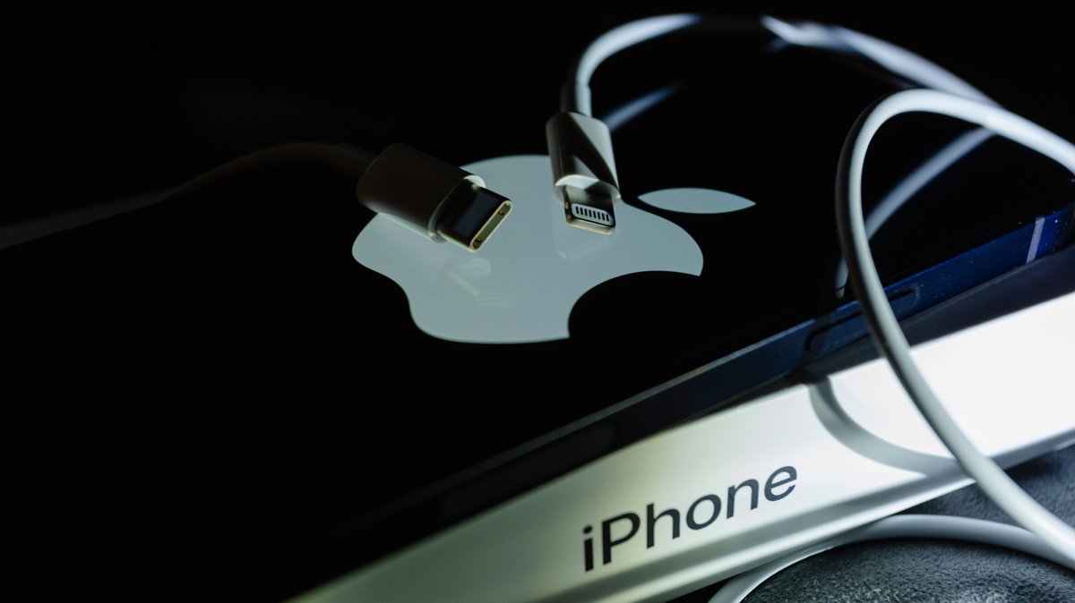 Je ein Kabel mit USB-C-Anschluss und eines mit Lightning liegen auf einem iPhone.