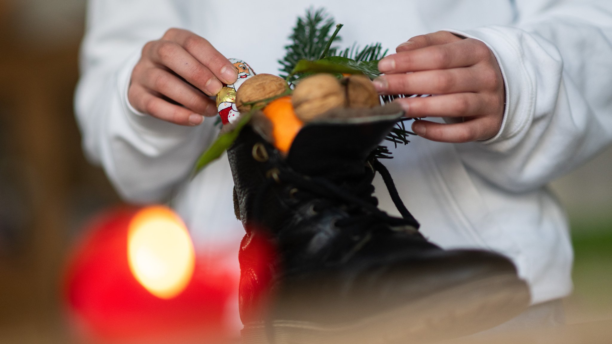 (Symbolbild) Mädchen packt am Nikolaustag Stiefel mit Nüssen und Schokonikolaus aus