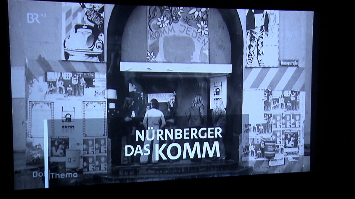 auf der Kinoleinwand ist der Titel der Doku "Radikal an der Basis – Das Nürnberger KOMM" zu sehen
