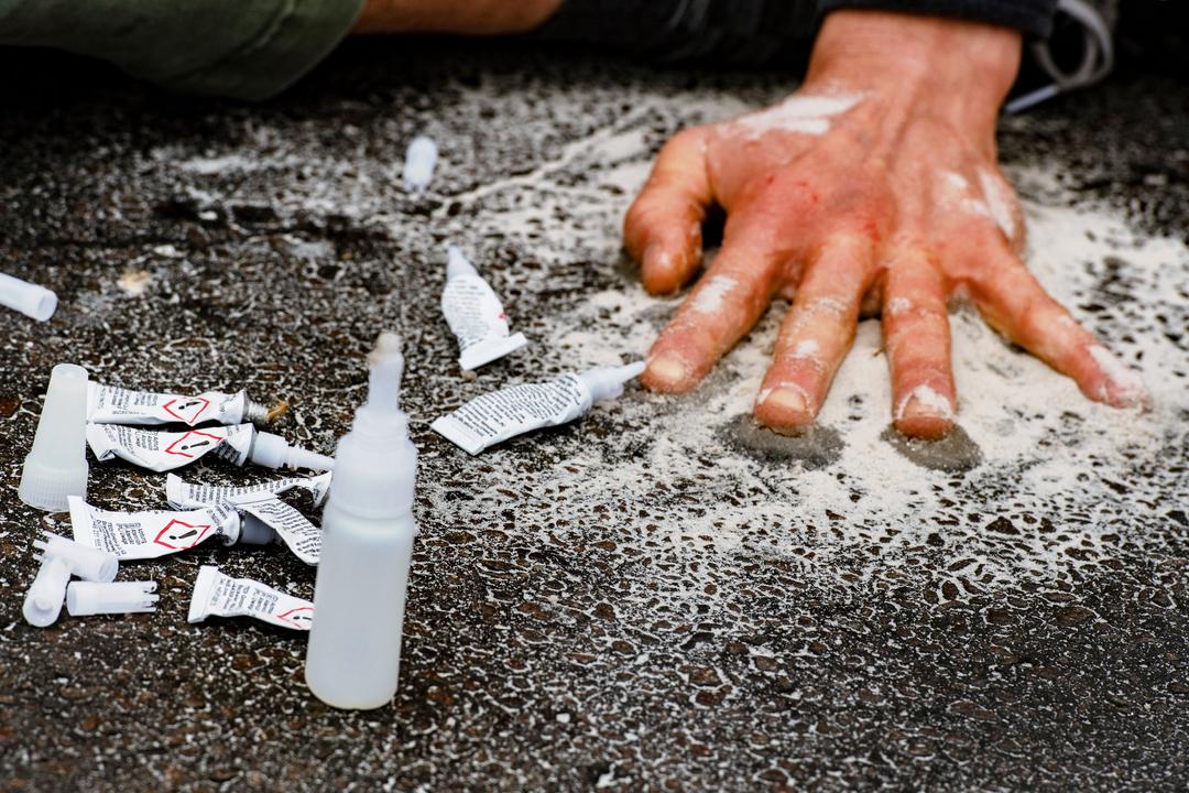 Ein Demonstrant klebt sich bei einer Straßenblockade der Letzten Generation mit einer Hand auf die Straße.