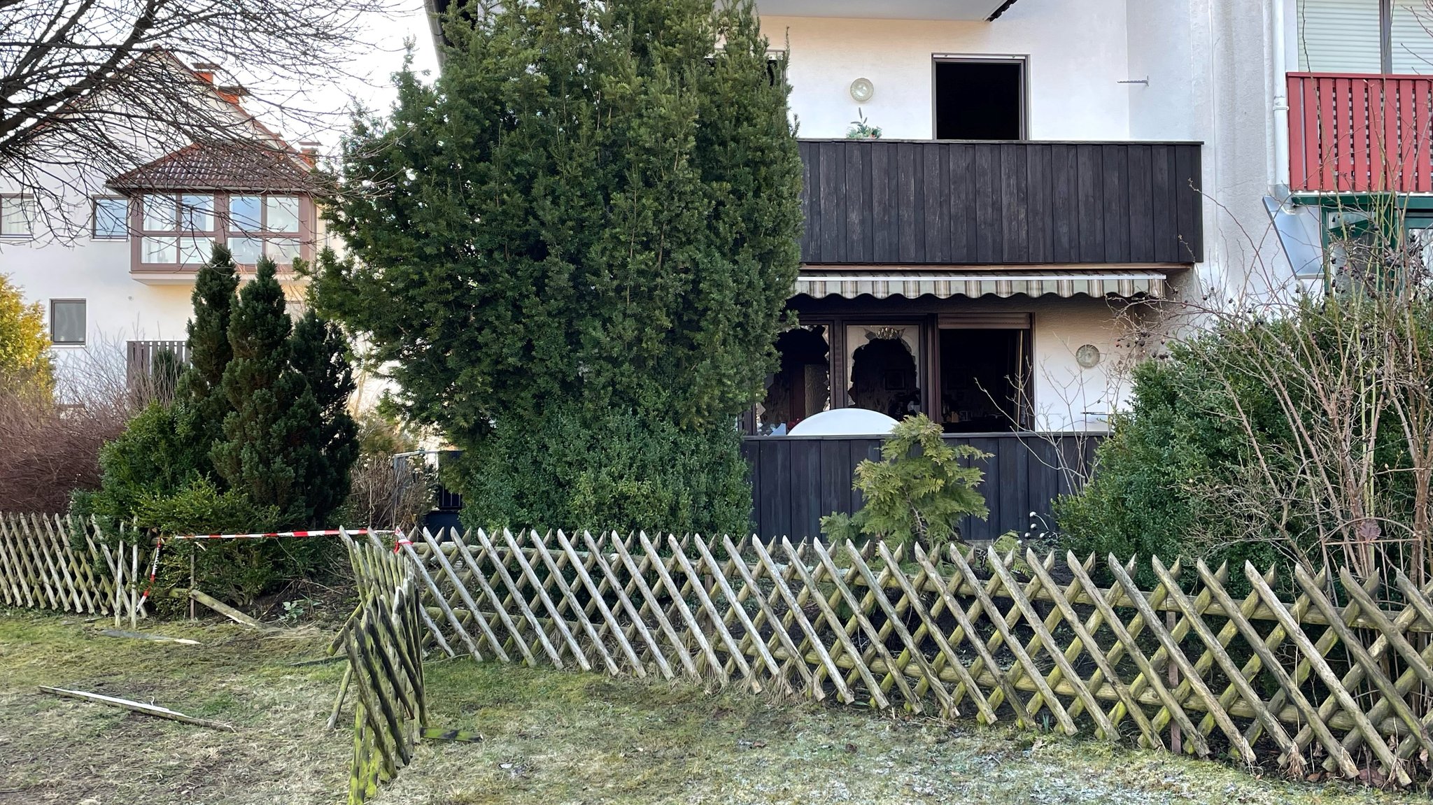 Zerstörter Gartenzaun vor einem Haus, dessen Fensterscheiben zerbrochen sind.