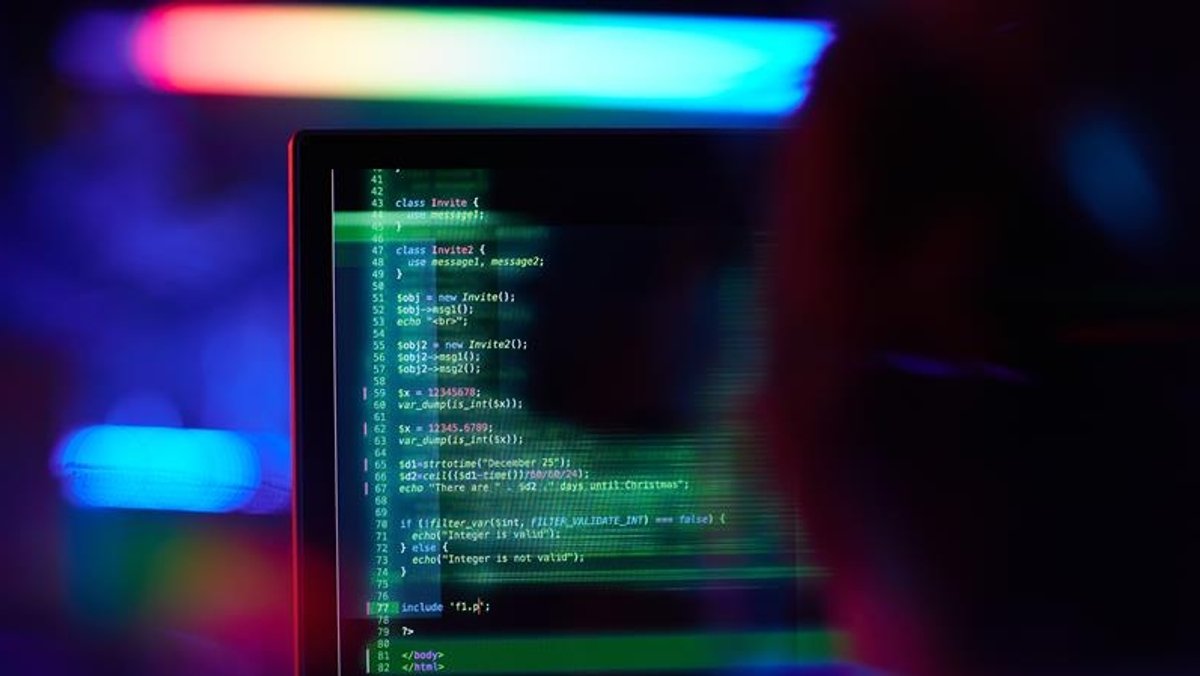 Eine Person sitzt vor einem Bildschirm, auf dem Programmier-Codes zu sehen sind.