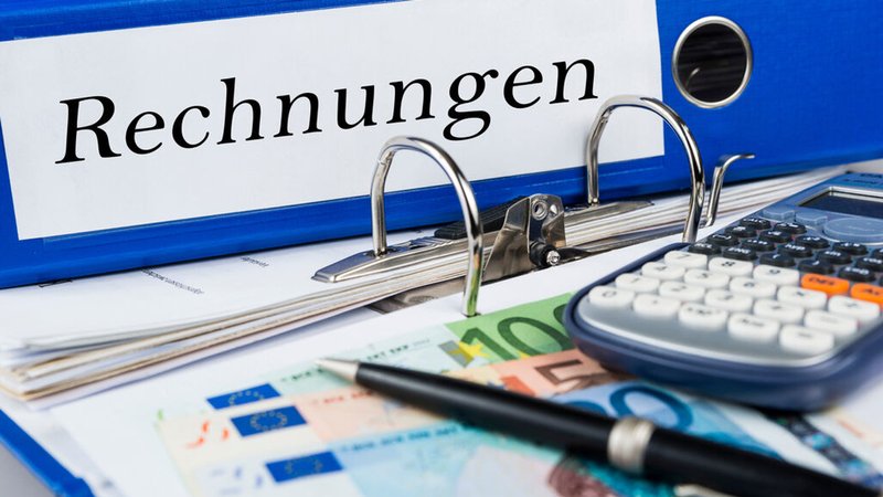 Ein Ordner mit der Aufschrift "Rechnungen", Bargeld und ein Taschenrechner liegen auf einem Tisch. | Bild: stock.adobe.com/marcus_hofmann Ein Ordner mit der Aufschrift "Rechnungen", Bargeld und ein Taschenrechner liegen auf einem Tisch.