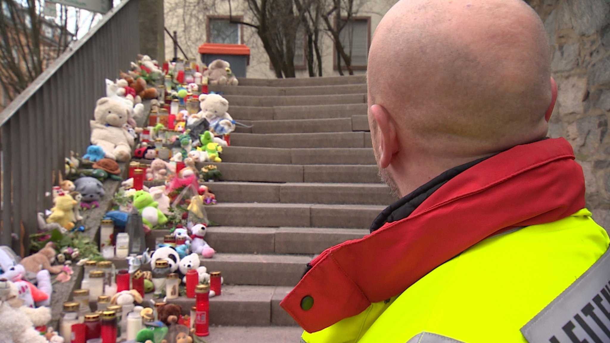 Kerzen und Kuscheltiere säumen die Treppe, die in den Park Schöntal in Aschaffenburg führt. Vor der Treppe steht Notarzt Daniel Merten in Dienstkleidung, mit dem Rücken zur Kamera.