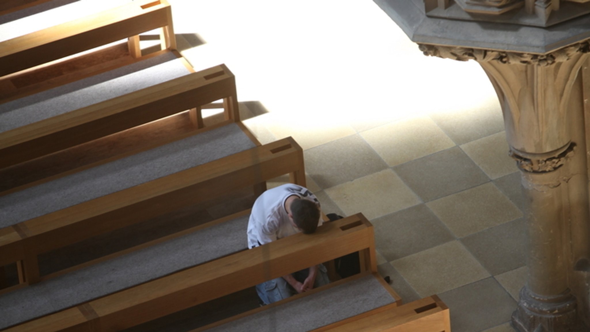 Ein Mann sitzt in einer Kirchenbank. Die anderen Bänke sind leer. 