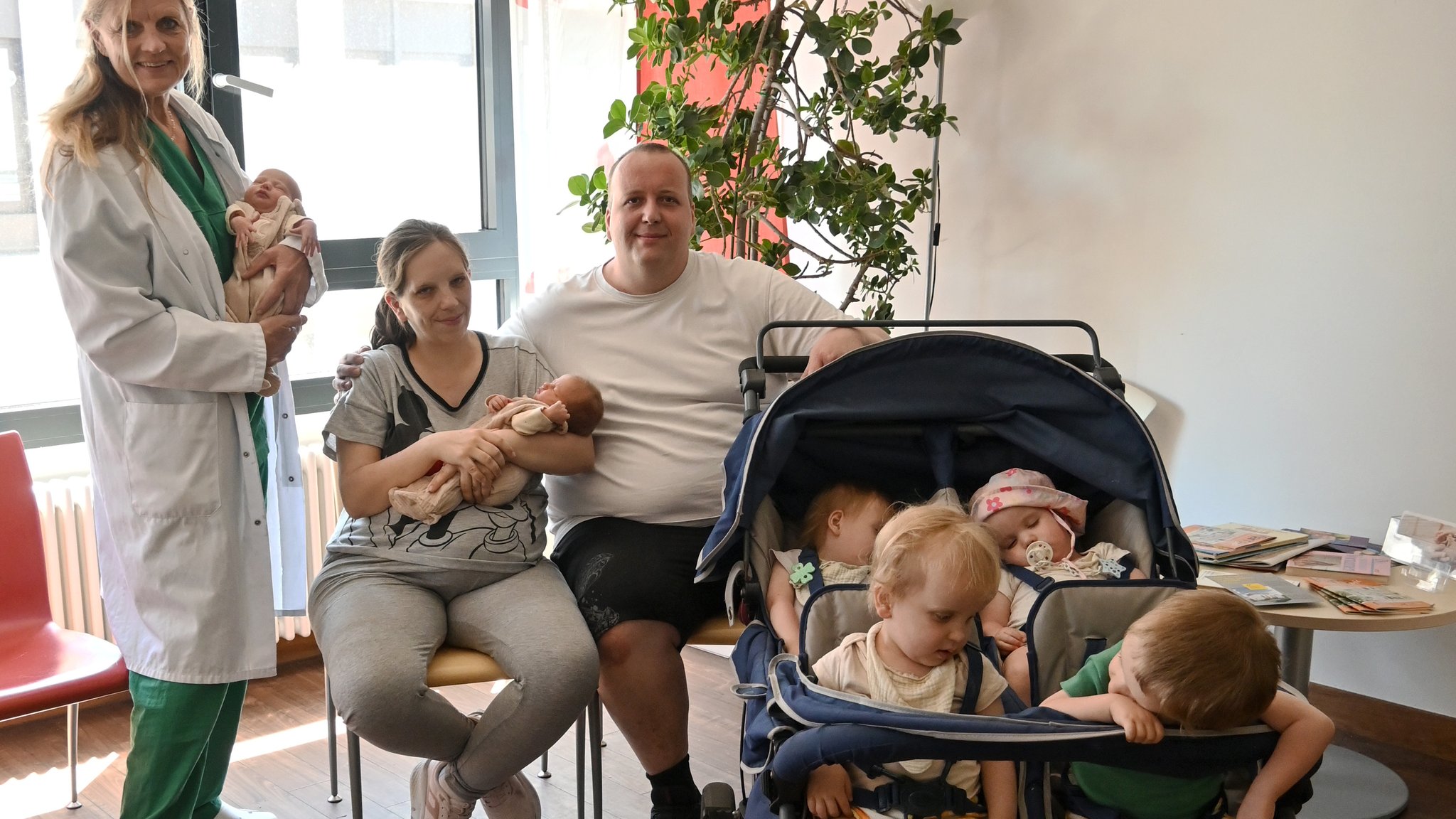 Eine Frau und ein Mann sitzen auf Stühlen. Neben ihnen steht ein Kinderwagen, in dem vier Kinder sitzen. Die Frau hat ein Baby auf dem Arm. Neben dem Paar steht eine Ärztin, die ein weiteres Baby im Arm hat. | Bild: Klinikum Fürth Eine Frau und ein Mann sitzen auf Stühlen. Neben ihnen steht ein Kinderwagen, in dem vier Kinder sitzen. Die Frau hat ein Baby auf dem Arm. Neben dem Paar steht eine Ärztin, die ein weiteres Baby im Arm hat.