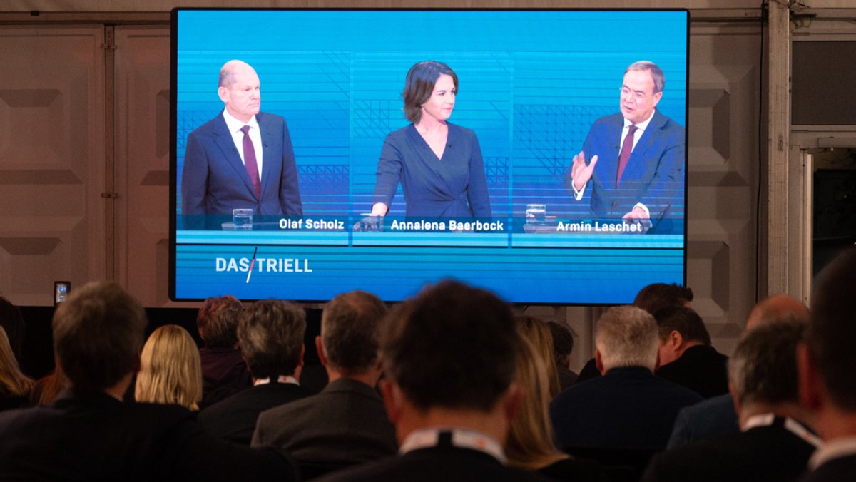 Scholz (SPD, l-r), Baerbock (Bündnis90/Die Grünen) und Laschet (CDU) sind während des Triells auf einem Bildschirm zu sehen.