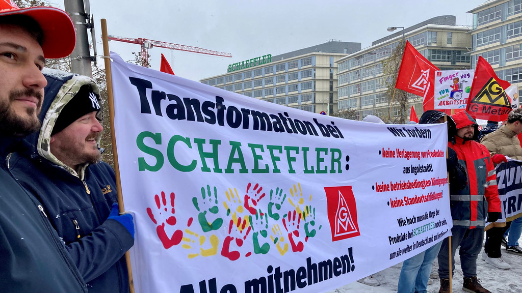 Menschen mit Fahnen und Transparenten protestieren vor dem Firmensitz  von Schaeffler in Herzogenaurach.