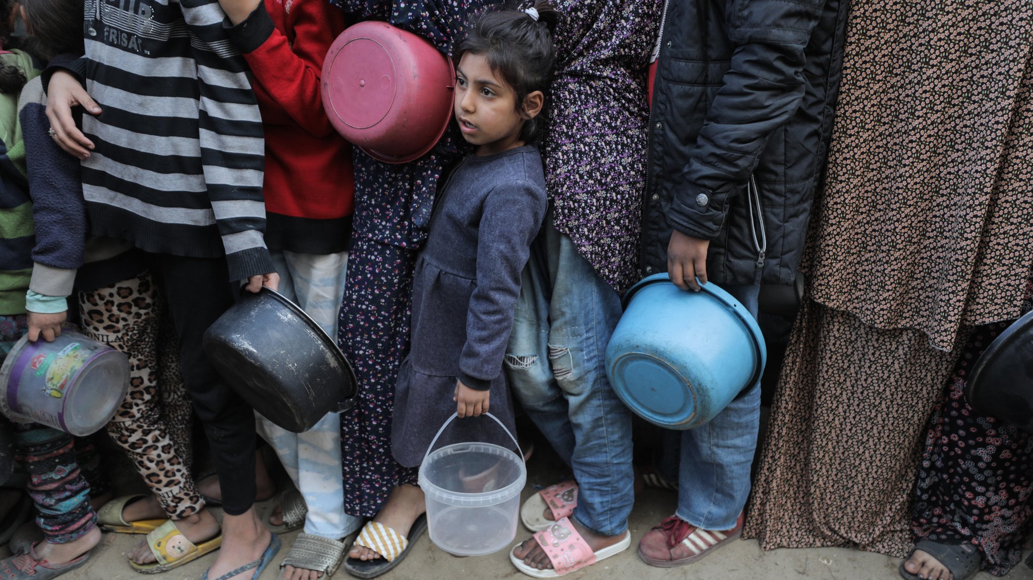 Menschen im Gazastreifen, darunter Kinder, warten mit leeren Behältern auf Nahrungsmittel einer Hilfsorganisation (Bild vom 22.11.24).