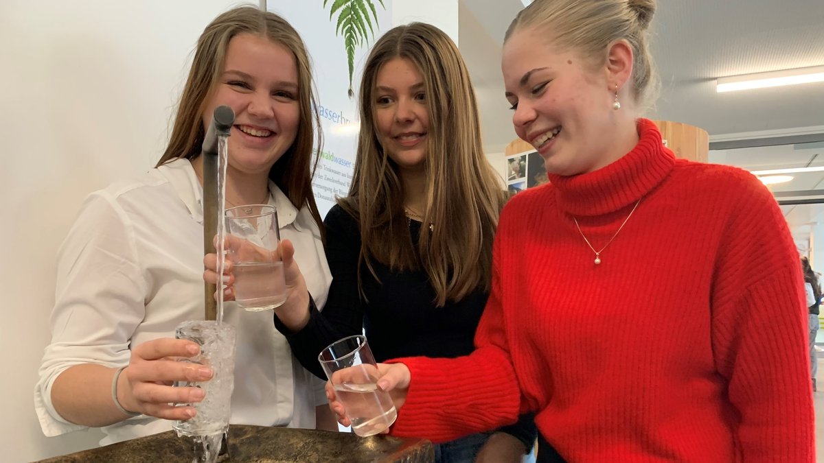 Drei Schülerinnen füllen ihre Gläser an einem Trinkwasserbrunnen