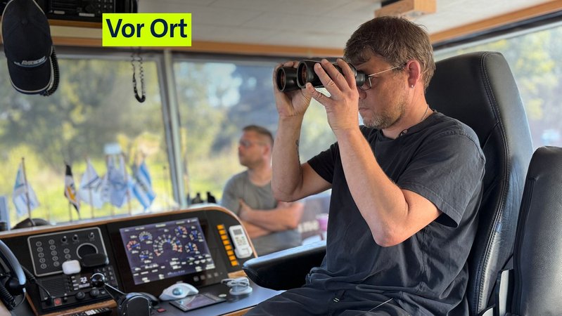 Binnenschiffer Florian Wichern schaut in seinem Cockpit durch ein Fernglas.  | Bild: BR/Pirmin Breninek Binnenschiffer Florian Wichern schaut in seinem Cockpit durch ein Fernglas.