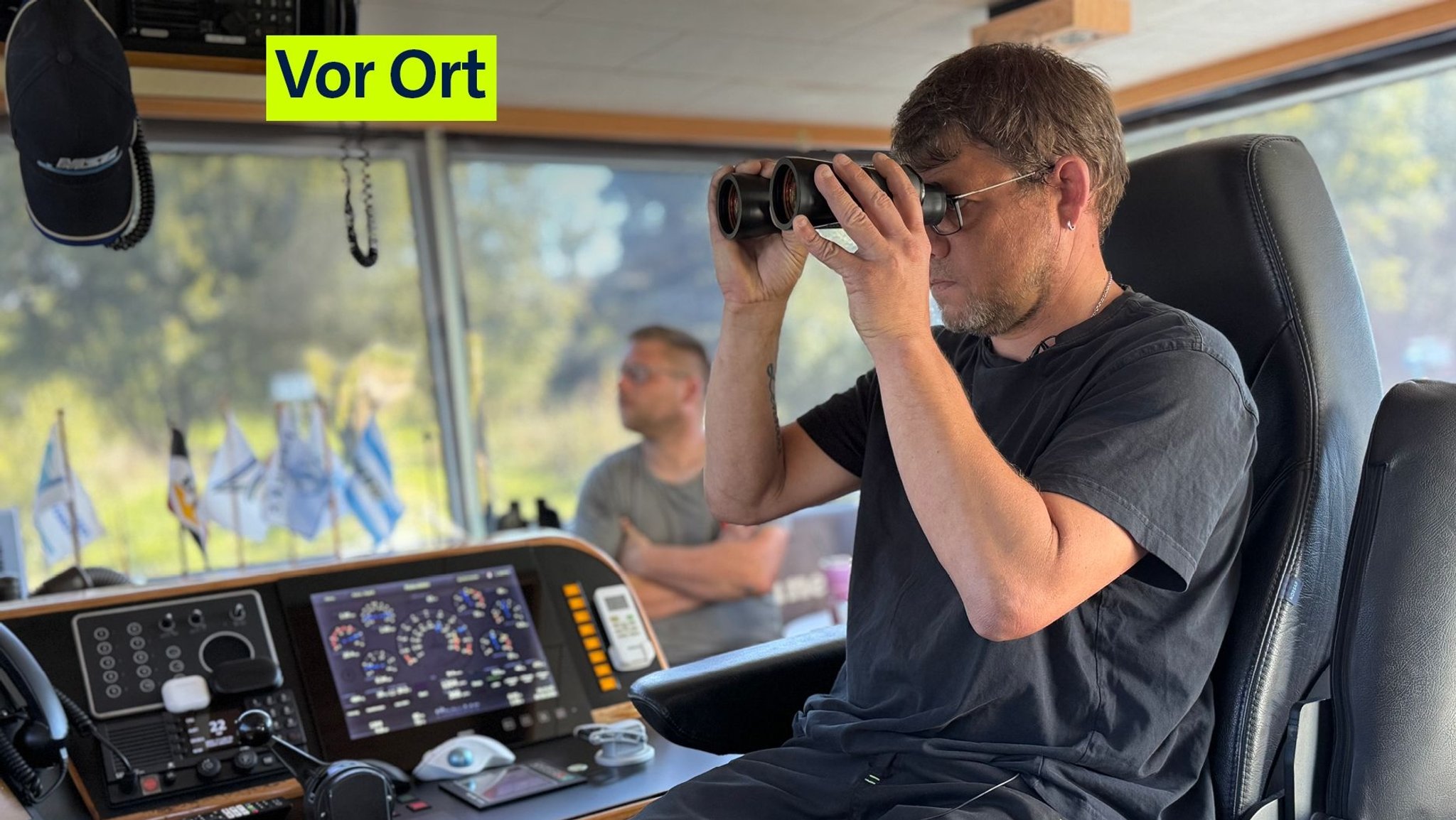 Binnenschiffer Florian Wichern schaut in seinem Cockpit durch ein Fernglas. 