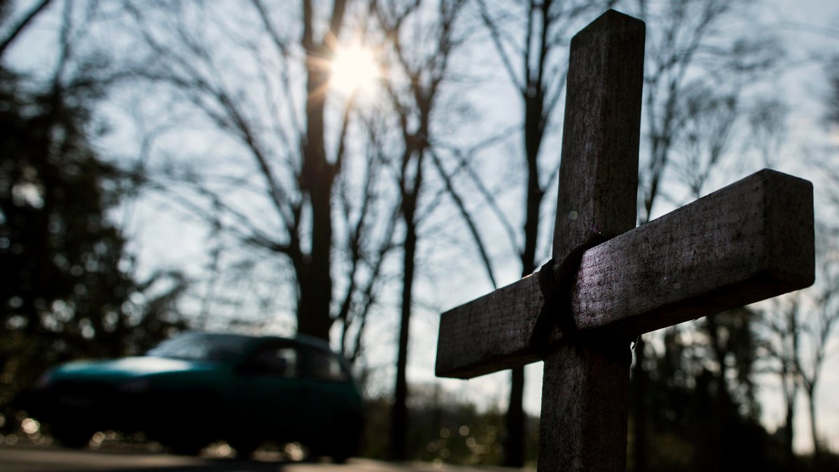 Ein Auto fährt an einem Kreuz zur Erinnerung an einen Verkehrstoten auf einer Landstraße vorbei