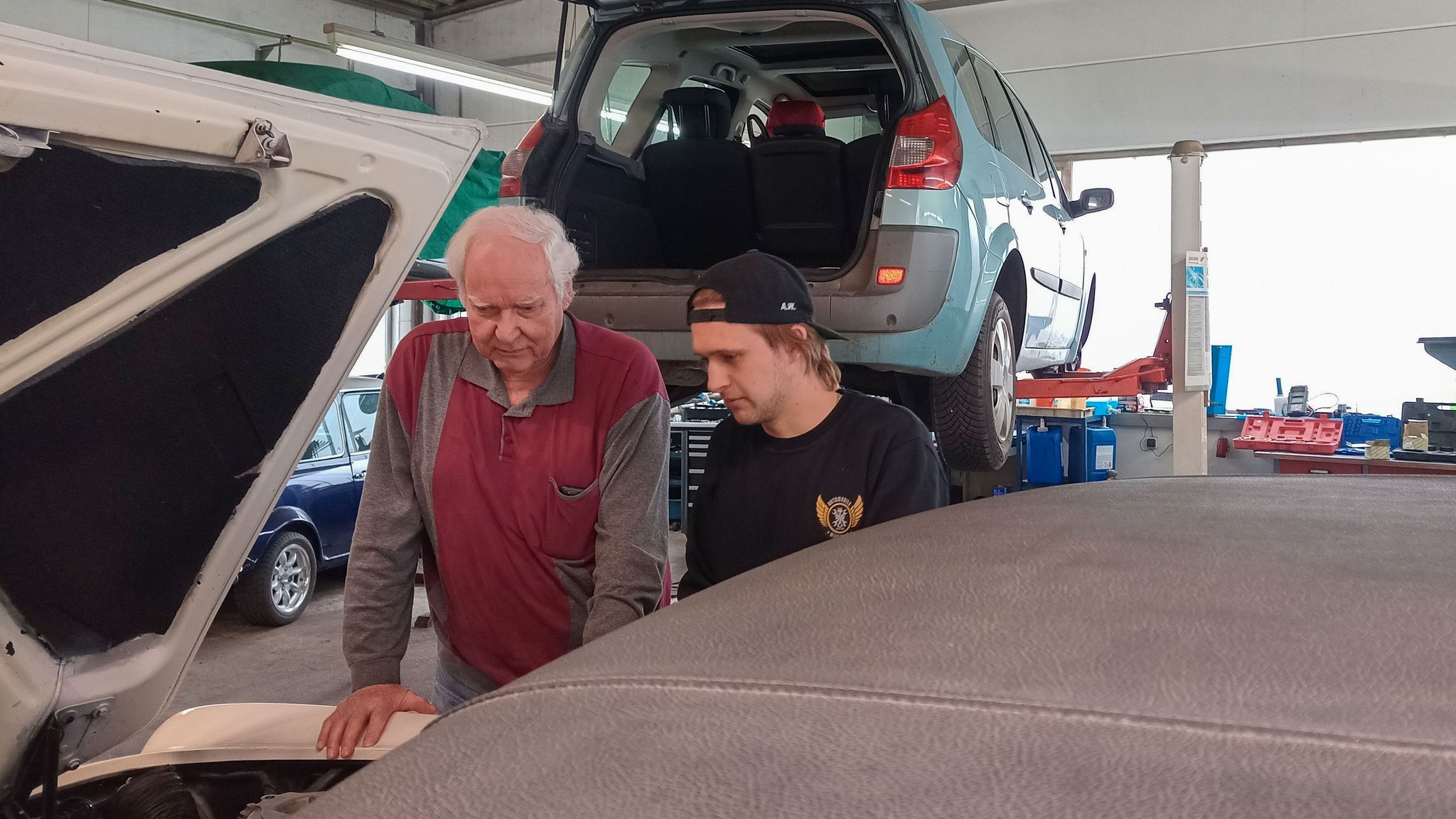 Zwei Männer schauen in einer Kfz-Werkstatt in den Motorraum eines Autos.