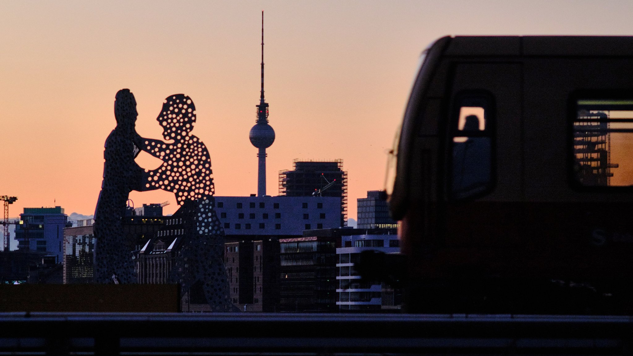 Berlin: Eine S-Bahn fährt in den Bahnhof Treptower-Park ein, vorbei am Berliner Fernsehturm und an der Skulptur "Molecule Man".