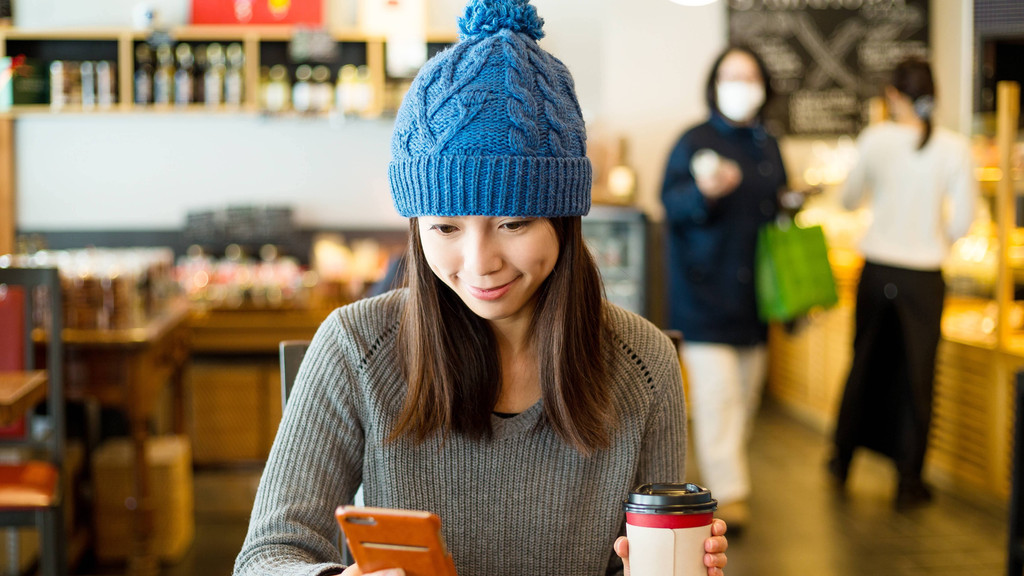 Junge Frau mit Mütze, Handy und warmem Getränk