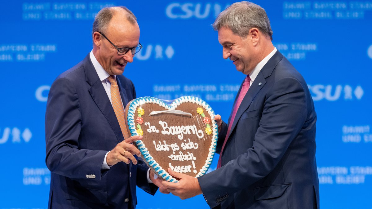 München, 23.09.23: CDU-Chef Merz (l.) kriegt von CSU-Chef Söder ein Lebkuchenherz mit der Aufschrift "In Bayern lebt es sich einfach besser!".