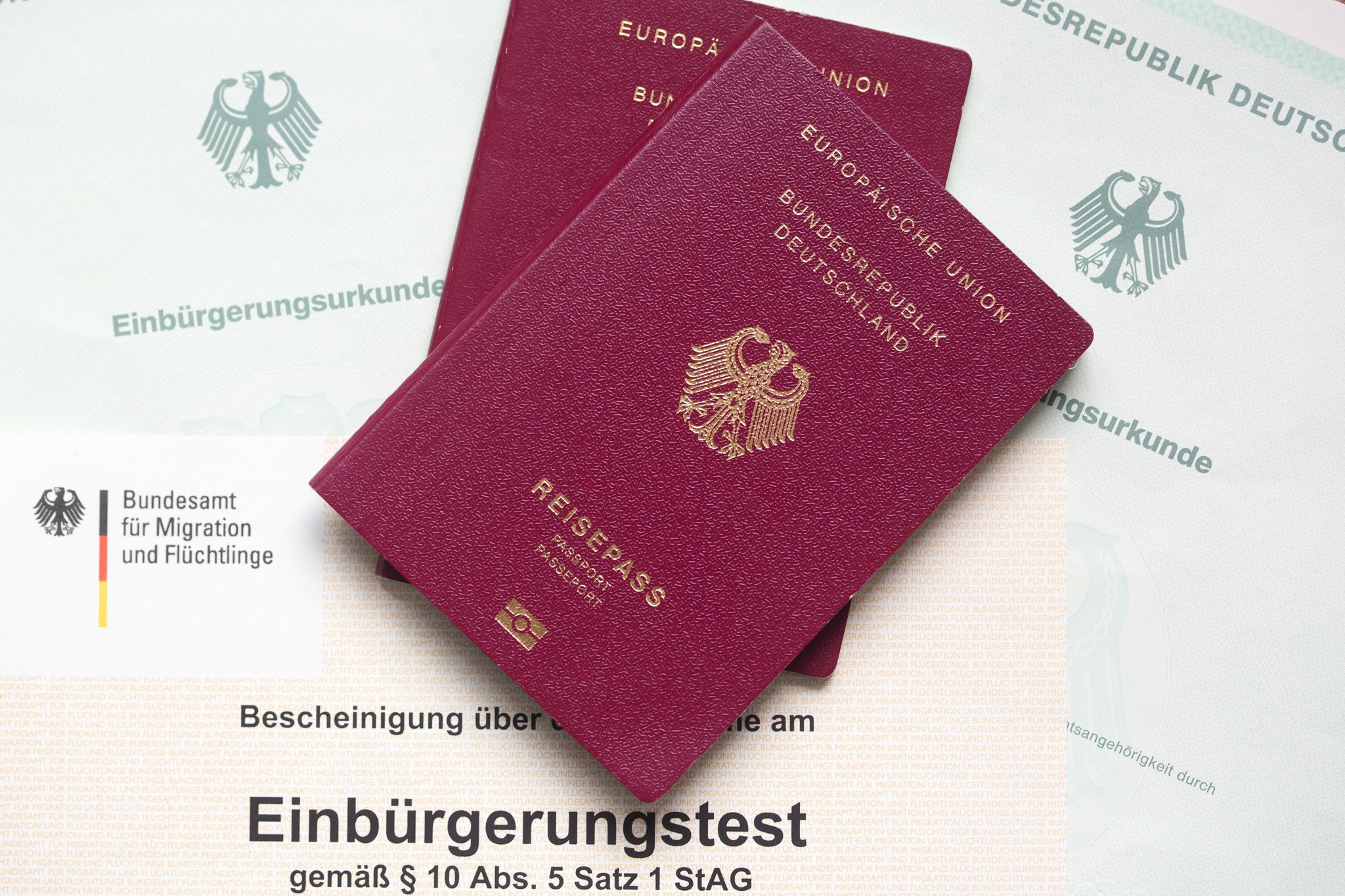 Zwei deutsche Reisepässe liegen auf Einbürgerungsurkunden der Bundesrepublik Deutschland sowie einer Bescheinigung über den bestandenen Einbürgerungstest.