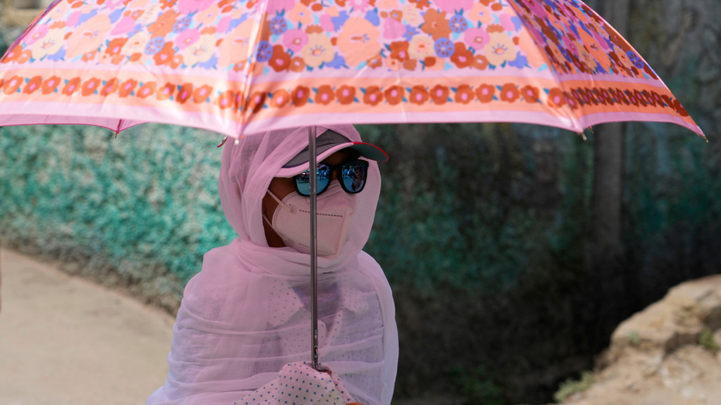 Hitzewelle in Indien und Pakistan im April 2022: Eine junge Frau schützt sich mit einem Regenschirm und einem Schal vor der Hitzewelle im Staat Uttar Pradesh in Indien. 