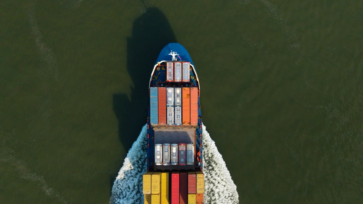 Ein mit bunten Containern beladener Frachter fährt auf einen niederländischen Hafen zu. 