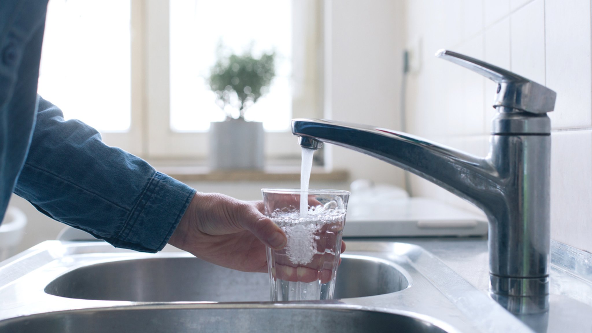 Jemand füllt am Wasserhahn ein Glas mit Leitungswasser.