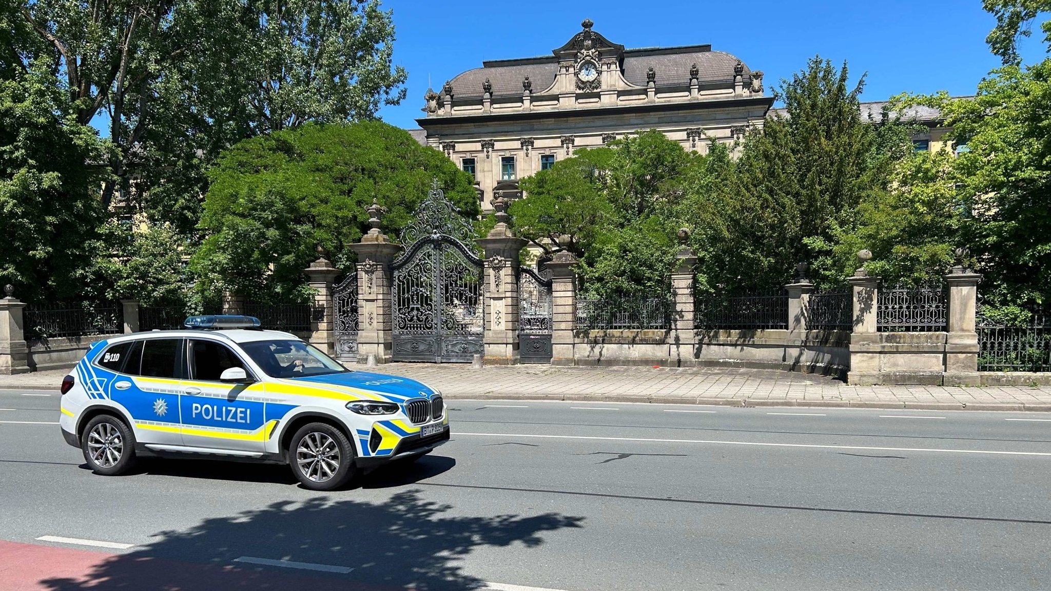 Ein Polizeiauto steht auf einer Straße vor einem großen, alten Gebäude, das von einem Mauerzaun umgeben ist. | Bild: BR/Markus Feulner Ein Polizeiauto steht auf einer Straße vor einem großen, alten Gebäude, das von einem Mauerzaun umgeben ist.