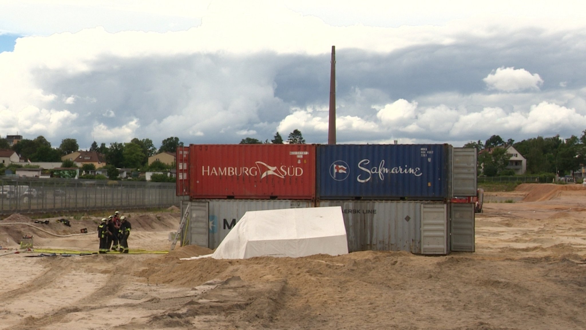 Weißes Zelt für den Sprengmeister auf einer Baustelle, dahinter mit Wasser gefüllte Schiffscontainer.