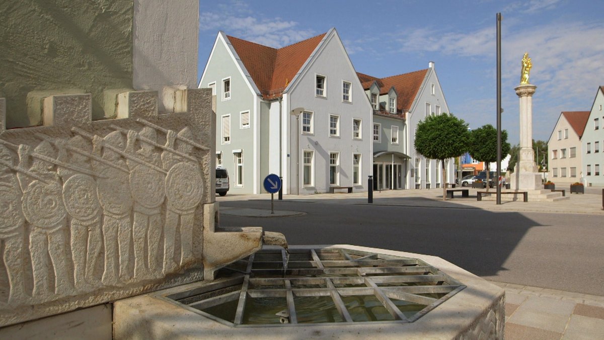 Die Ortsmitte in Großmehring mit zentralem Platz, Mariensäule und Fahnenstange. Im Vordergrund ein Brunnen.