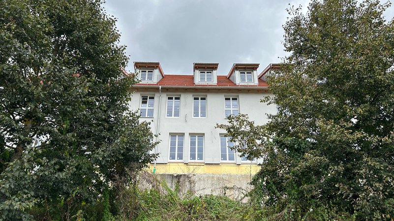 Im Vordergrund links und rechts Bäume, dazwischen im Hintergrund ein Wohnhaus | Bild: BR/Andreas Wenleder Im Vordergrund links und rechts Bäume, dazwischen im Hintergrund ein Wohnhaus