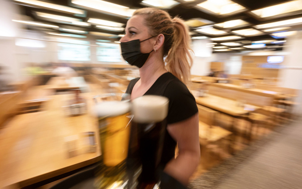 Eine Kellnerin läuft mit zwei Biergläsern durch ein Restaurant. Sie trägt einen Mund-Nasen-Schutz.