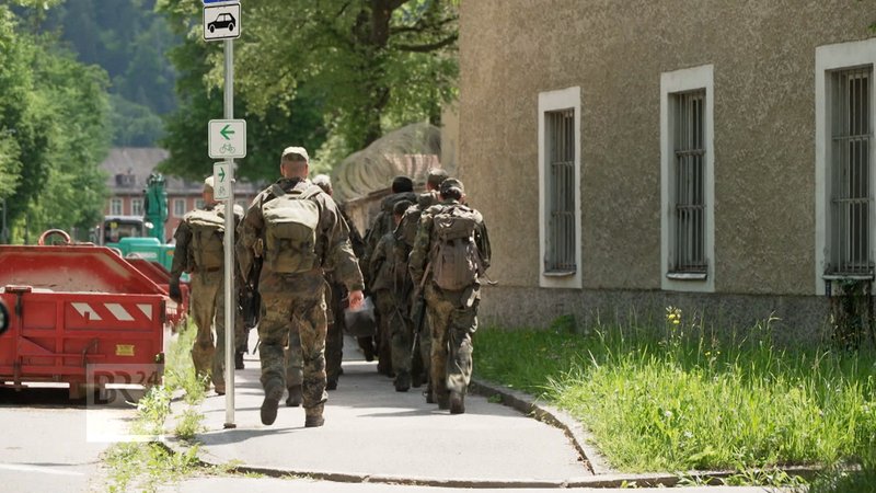 Soldaten und Soldatinnen marschieren neben einem Haus.