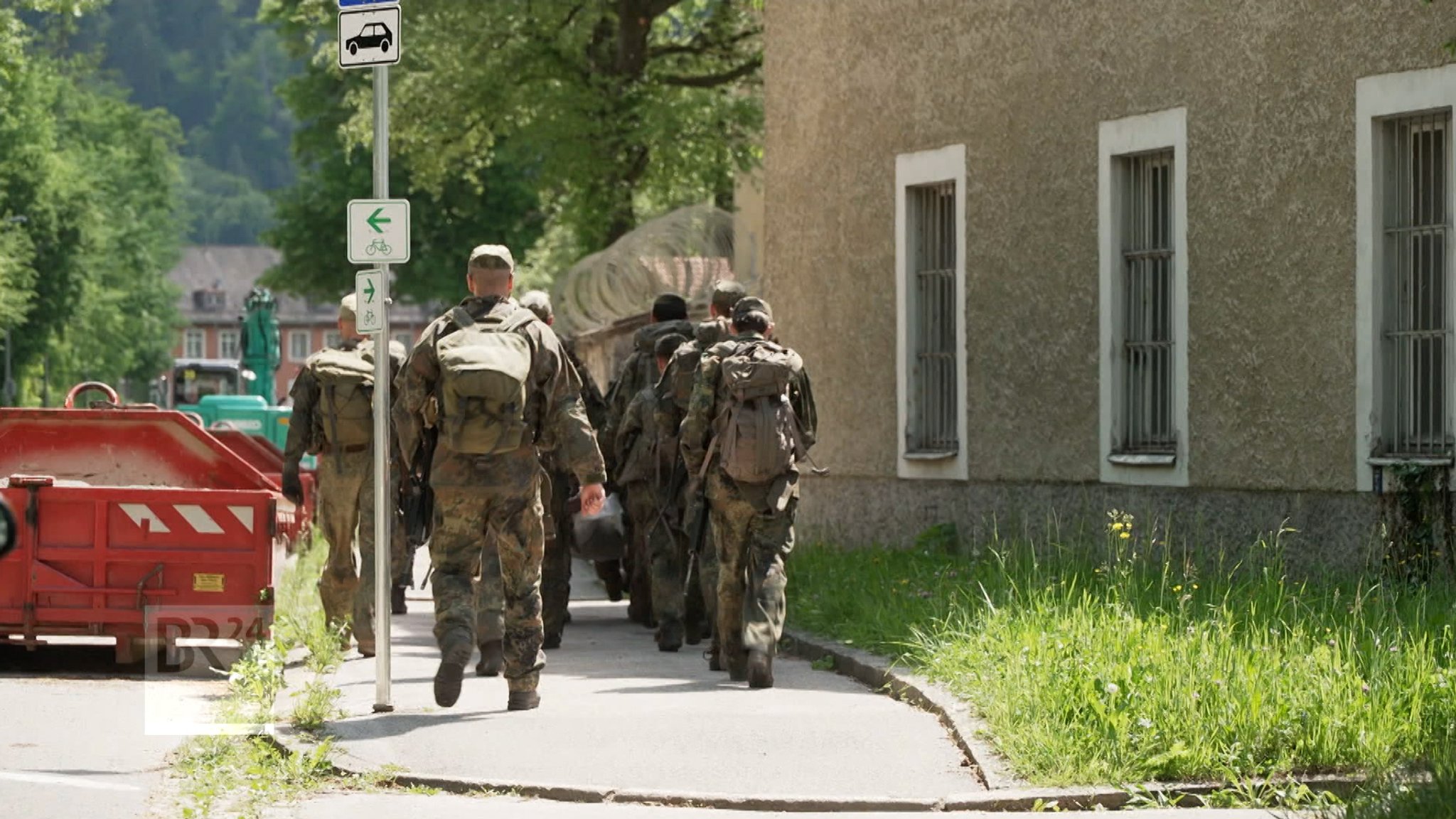 Soldaten und Soldatinnen marschieren neben einem Haus.