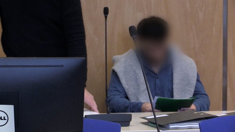 Ein Mann, dessen Gesicht für Fotografen unkenntlich gemacht ist, sitzt im Gerichtssaal auf der Anklagebank. 
