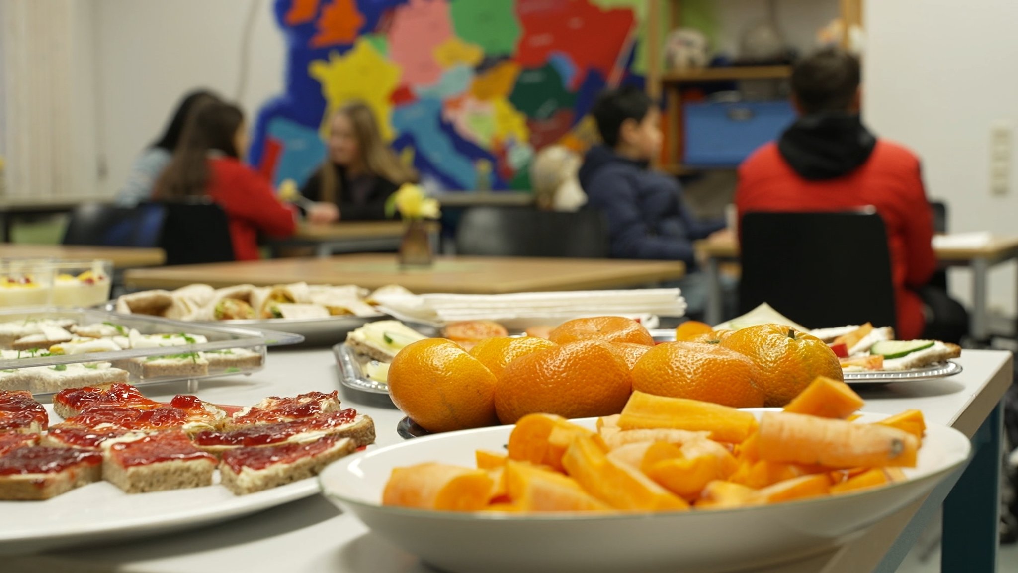 Gesunde Lebensmittel stehen auf einem Tisch im Kindergarten. Kinder sind im Hintergrund zu sehen. 