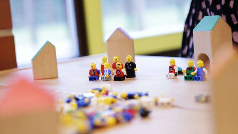 Legofiguren sitzen, stehen und liegen in einem Kindergarten auf einem Tisch. Dazu Holzklötze, die wie Häuser aussehen. | Bild: BR/Isabel Pogner Legofiguren sitzen, stehen und liegen in einem Kindergarten auf einem Tisch. Dazu Holzklötze, die wie Häuser aussehen.