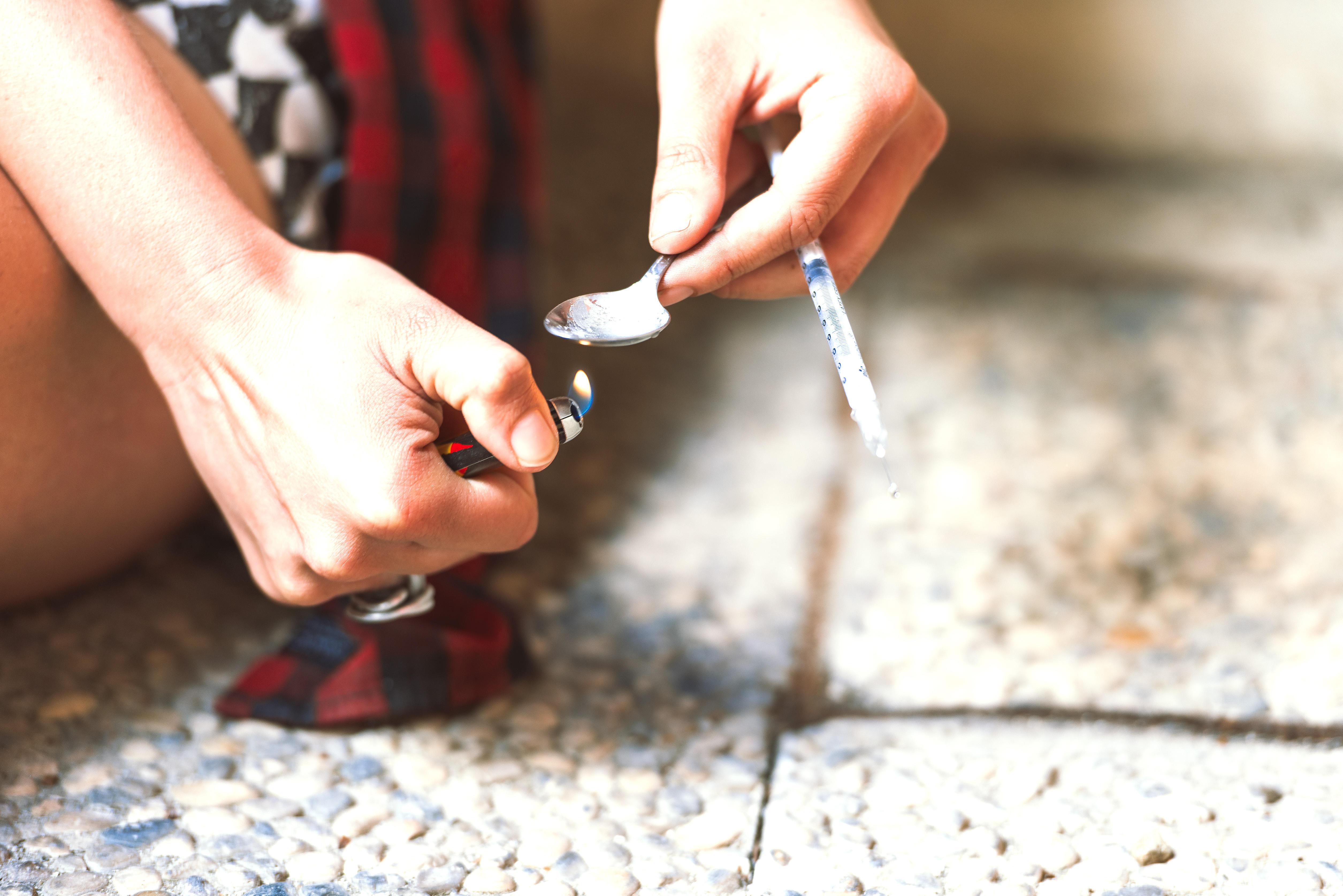 Hand mit Feuerzeug unter Löffel und Spritze