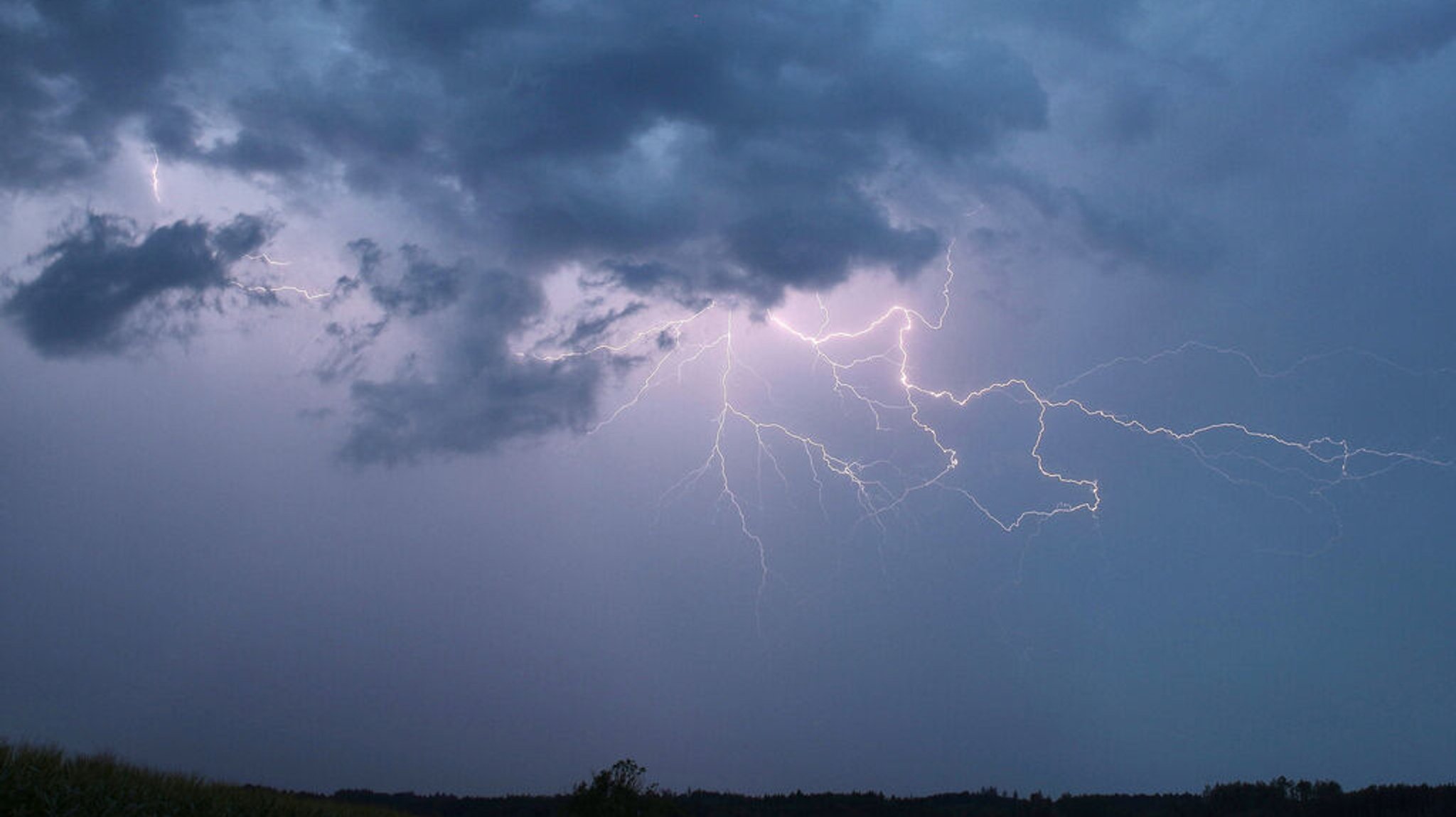 Ein Blitz zuckt bei einem Sommergewitter am abendlichen Himmel. 