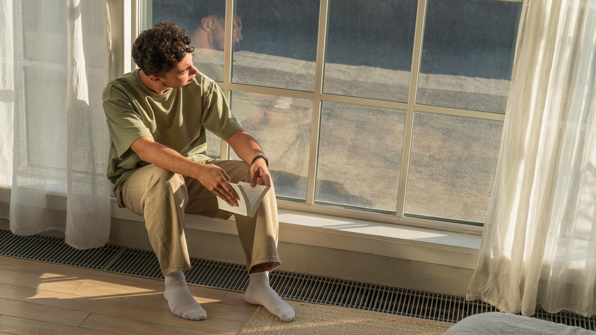 Symbolbild Einsamkeit junge Menschen. Junger Mann sitzt mit Buch am Fenster.