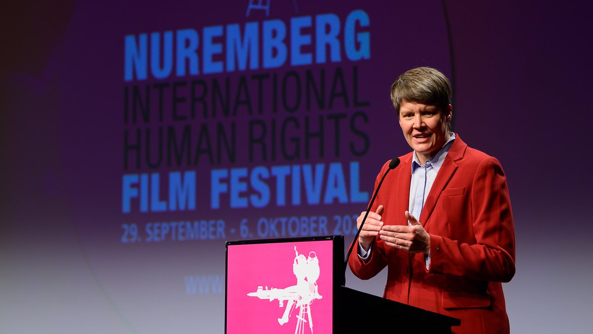 Frau im roten Anzug steht vor einem Pult, im Hintergrund die Aufschrift "Nuremberg International Human Rights Film Festival".